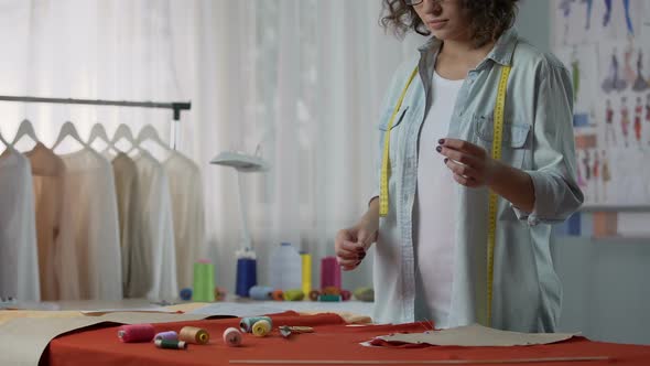 Seamstress putting thread in needle, starting to sew parts of clothes together