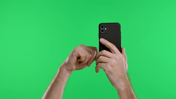 Male Hands Hold a Smartphone Vertically Against the Background of a Green Screen Chroma Key