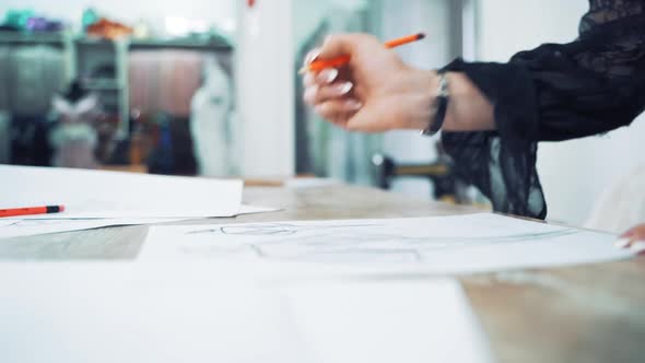 Hands of a professional tailor is drawing a sketch with a sharp pencil on a table.