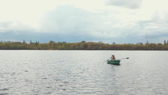 A Man and a Young Woman Ride a Boat on a Calm Lake Surrounded By Trees