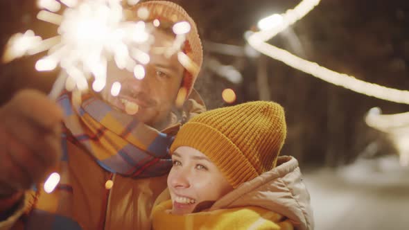 Affectionate Couple Holding Christmas Sparkler and Kissing Outdoors
