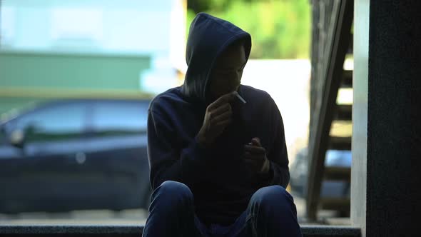 African American Teenager Cautiously Looking Around, Hiding to Smoke Cigarette