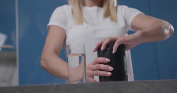 A Woman's Hand Pours Powder From a Black Jar Into a Glass