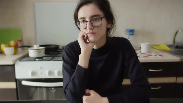Bored Girl Is Sitting in the Kitchen with Glasses and Thinking About Something