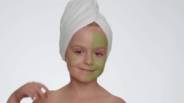 Beautiful Smiling Child Girl Kid in Towel on Head Applying Cleansing Moisturizing Green Mask on Face