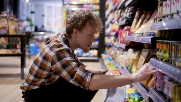 Busystore Clerk Working at the Supermarket He is Resorting Items on a Shelf Writing Down the Lack of
