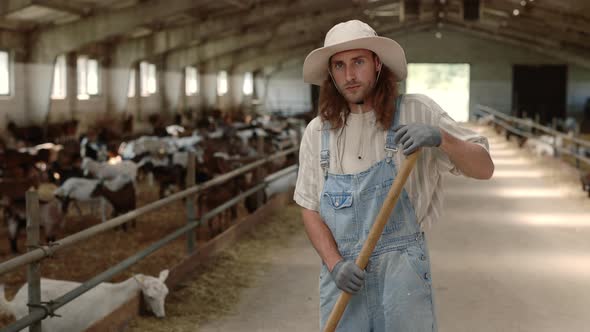 Caucasian Man in Overalls and Hat Cleaning Farm Goat