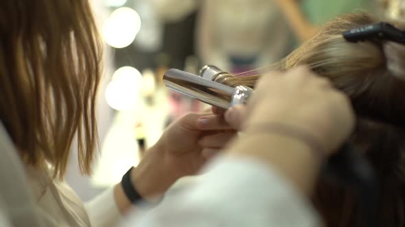 Closeup of Hands of Hairdresser Curling Long Hair with Curling Tongs