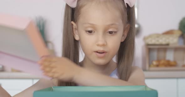 Close-up Face of Amazed Caucasian Girl Opening Glowing Gift and Looking Inside. Portrait of Charming