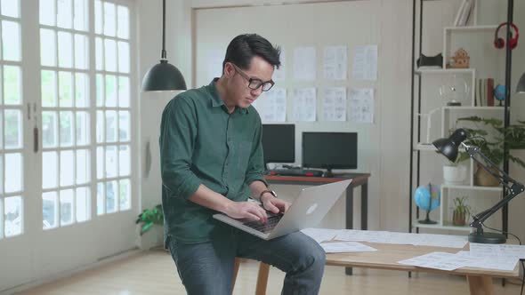 Creative Designer Sits On His Desk Holds Laptop On The Knees And Working On The Project