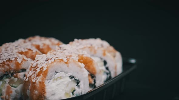 Sushi Rolls Rotating in Plastic Box on Black Background