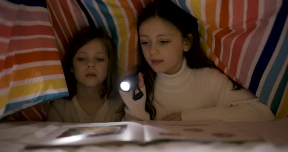 Two happy girls reading a book on the bed