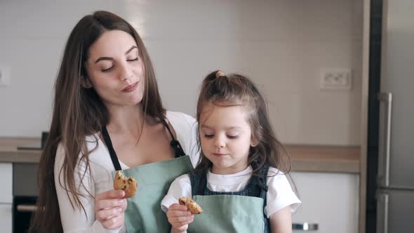 Pretty Mother and a Daughter Are Eating Cookies in a Kitchen