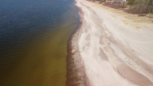 Aerial view of sea waves crashing into the beach with white sand on a sunny spring day, Baltic sea,