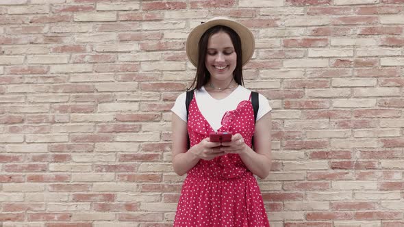 Trendy Hipster Tourist Using Mobile Phone While Standing Over Brick Wall