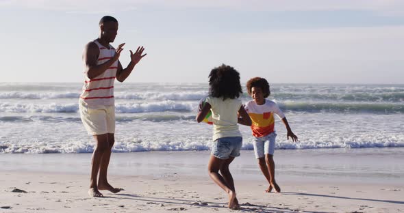 African american father and his children playing with a ball on the beach