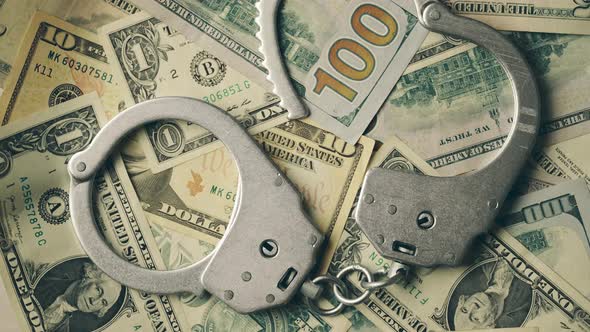 Close Up of Rotation Metal Handcuffs Over Stack of Dollar Banknotes