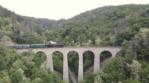 Stone viaduct in valley with a passing steam engine train,aerial zoom.