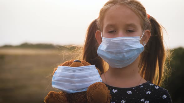 Sad Little Girl and Teddy Bear with Surgical Mask at Sunset, A Child Holding Her Teddy Bear During