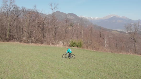 Aerial slow motion: man having fun by riding mountain bike in the grass on sunny day, scenic alpine