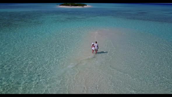 Two people tanning on beautiful coastline beach voyage by aqua blue ocean with white sand background