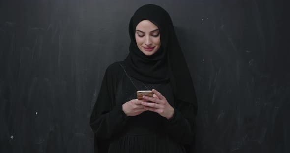 Modern Muslim Woman Using Smart Phone Over Black Chalkboard