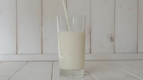 Close-up of Milk Being Poured Into a Glass on a Light Wooden Background.