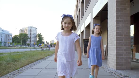 Two Cute Little Girls Are Walking Along the City Streets at Sunset