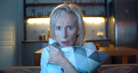 Close Up of Aged Woman Feeling Scared Watching Horror Movie on Tv and Hugging Pillow