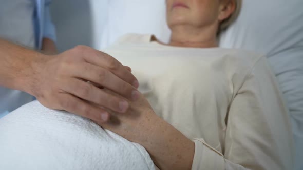 Loving Son Supporting and Comforting Terminally-Ill Mother in Her Hospital Ward