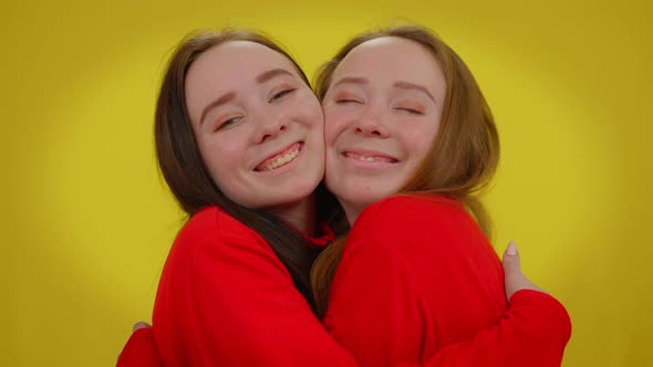 Smiling Twin Sisters Hugging Looking at Camera Posing at Yellow Background