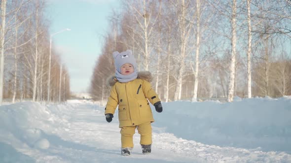 Toddler 15-20 months in yellow warm clothes walking along a path in a winter park