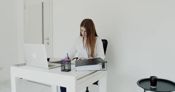 Young Girl Working with Laptop Writing in Notebook at Table in Office