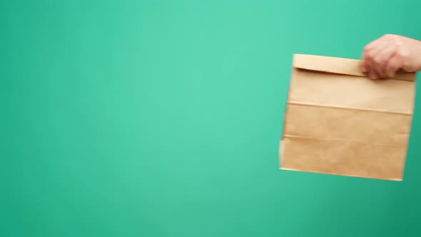 Courier in Gloves Passing Craft Shopping Bag with Delivery Against Mint Background