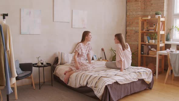 Happy Twin Sisters Sitting on Bed and Chatting