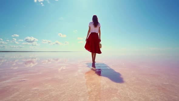 Woman Tourist Walking on Bright Pink Water Calm Water Surface of Lake and Blue Sky