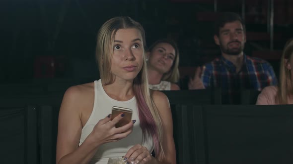 Woman with Smartphone Reading Message in Movie Theater