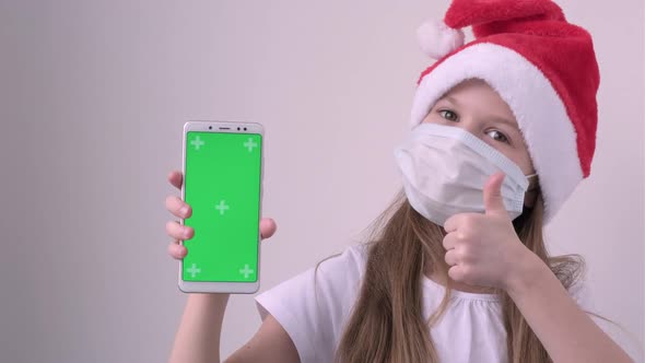 Little Girl in Christmas Santa Hat on White Background Wearing Surgical Mask Due to Coronavirus