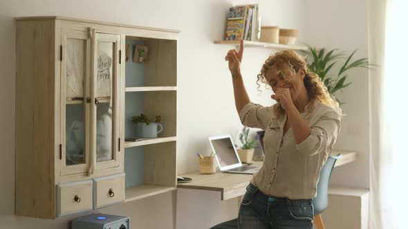 Excited and joyful middle age woman dancing at home singing a song for happiness