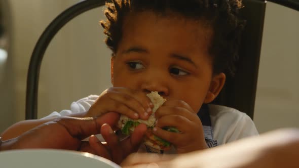 Close-up of cute little black son eating food at dinning table in kitchen of comfortable home 4k