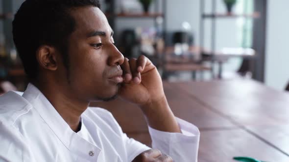 Close-up Face of Overworked Young African Black Male Doctor Drinking Coffee During Working on Laptop