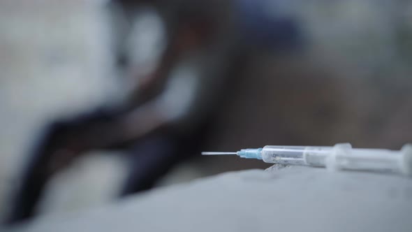 Close-up of Syringe with Blurred Junkie Writhing at the Background. Unrecognizable Overdosed Drug