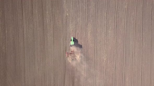 Top Down Aerial View of Green Tractor Cultivating Ground and Seeding a Dry Field