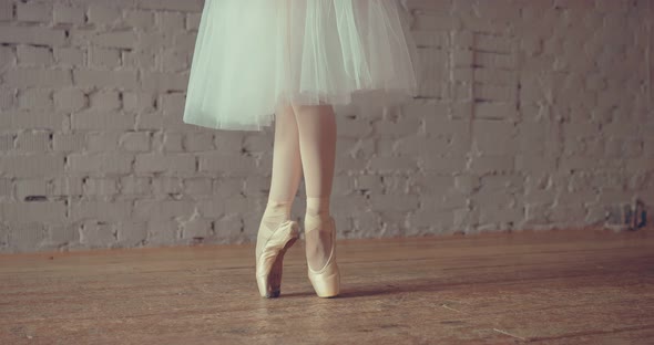 Professional Dancer in a White Skirt and Pointe Makes Ballet Movements with Her Legs