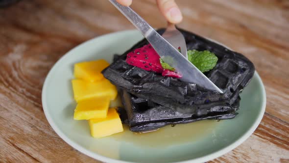 Top View of Hands Cutting Black Belgian Vegan Waffles with Silver Cutlery