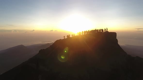 Reveal shot of sunrise over peoples silhouettes on the top of Mt Rinjani