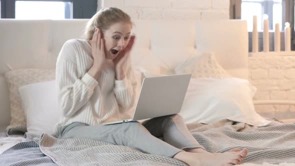 Amazed Young Woman Surprised by Results on Laptop in Bed