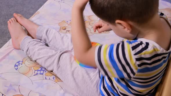 A Child of 4 Years Plays with Pop It in the Room on a Bed