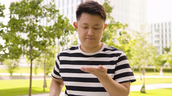 A Young Asian Man Applies Disinfectant Gel on His Hands and Smiles at the Camera in an Urban Area