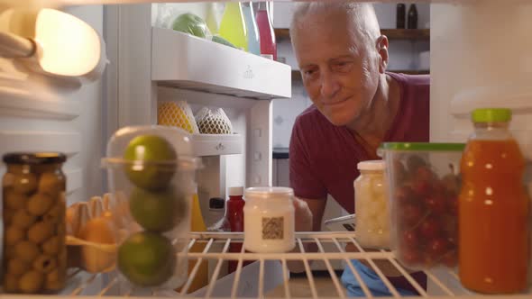 Senior Man Taking Yogurt From Fridge for Snack Checking Expiry Data